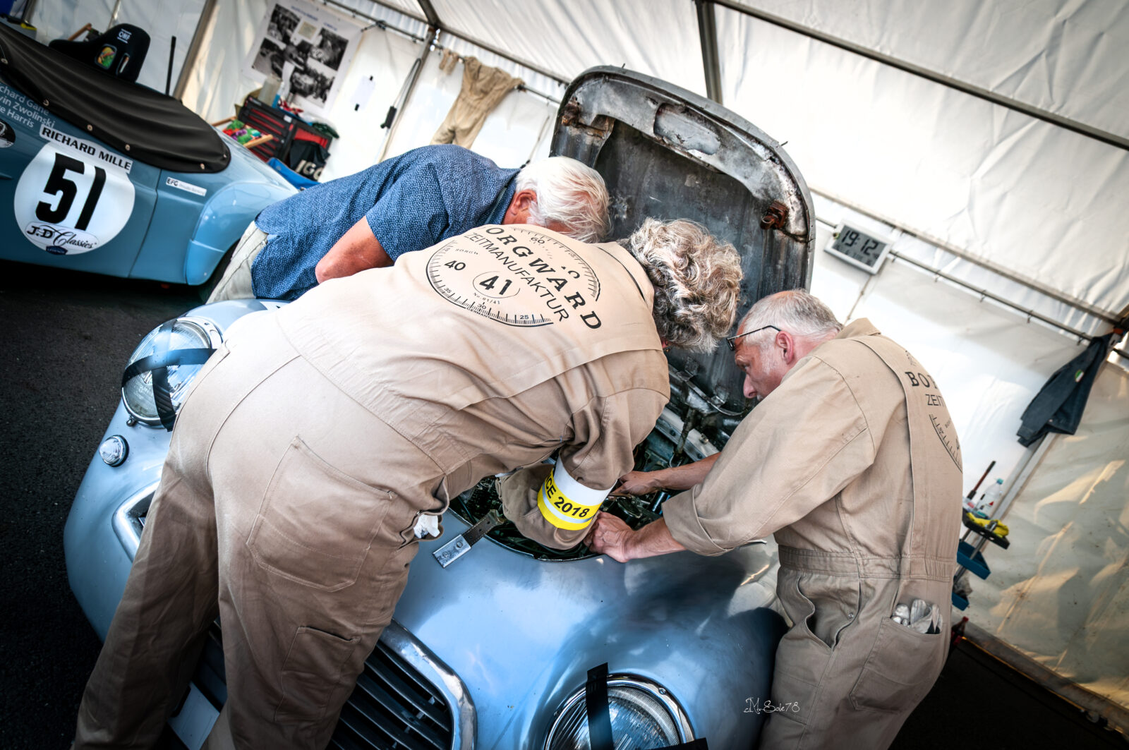 Meccanici in tuta al lavoro sul motore di un'auto da corsa d'epoca ai box di Le Mans
