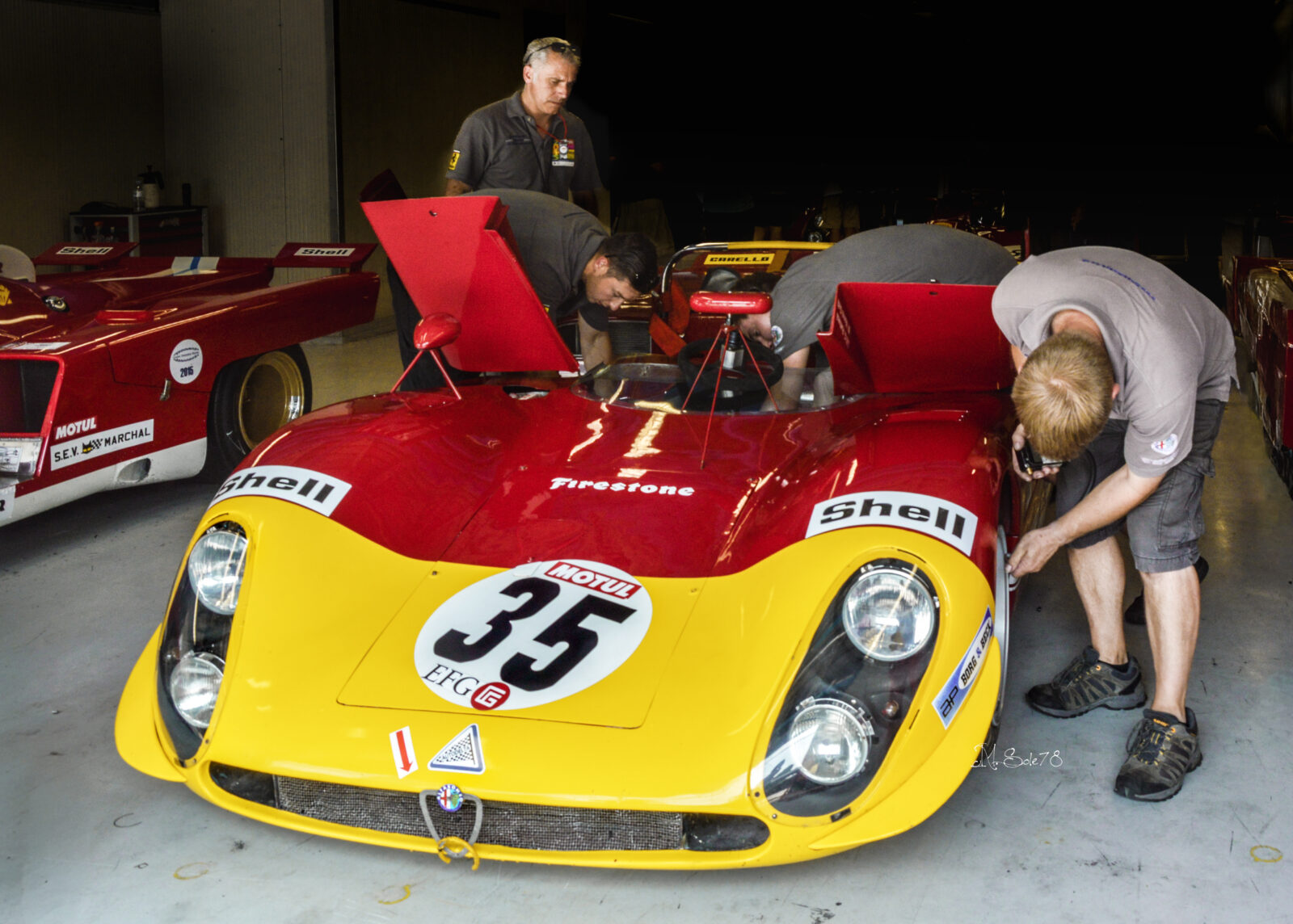 Meccanici al lavoro su Alfa Romeo 33/3 rossa e gialla numero 35 nel box a Monza